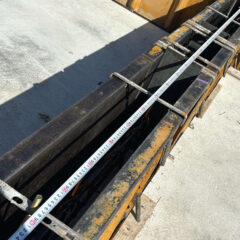 Metal formwork on a concrete slab with a tape measure stretched across to show dimensions.”] ,