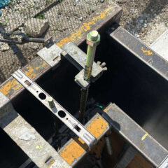 Close-up of metal formwork and a threaded rod secured with a nut and clamp for concrete pouring.