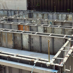Grid of metal and wood formwork panels for a building foundation, with braces, stakes, and pipelines ready for concrete