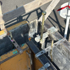 Close-up of a concrete formwork setup with steel rebar, clamps, and a level, supported by wooden planks and metal braces for a poured wall.