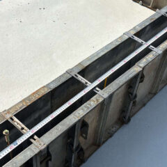 Metal formwork with a measuring tape laid across the top, showing a construction edge and clamps along a concrete slab edge.