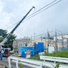 Construction site with a large crane lifting a beam over an unfinished wooden building, scaffolding around it.
