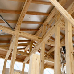 Interior view of a wooden-framed construction site with exposed studs and beams forming a skeletal roof.