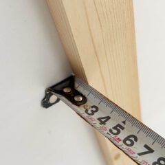 Close-up of a light wood plank being measured with a tape measure, showing the edge around 4 inches from the start (illustrating measurement).