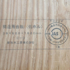 Wooden plywood panel with a Japanese stamp and a circular JAS certification seal visible on the grain