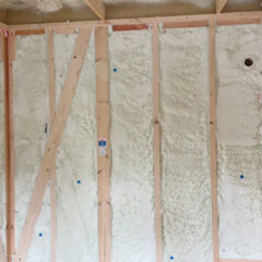 Interior wall framing under construction with vertical studs and white spray foam insulation between them. A diagonal brace runs across the left side of the wall.