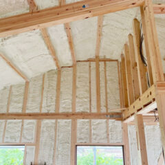 Interior of a framed attic with spray foam insulation between wooden studs and exposed ceiling joists (unfinished construction).