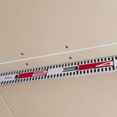 Measuring tape laid along a beige drywall surface with screws, showing the 2–3 inch range for alignment.