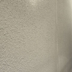 Beige stucco exterior wall with rough textured surface; a small structure or railing is visible on the right edge.