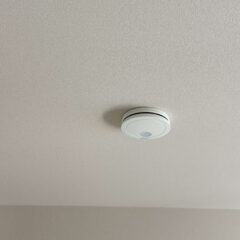 White circular smoke detector mounted on a textured ceiling in a beige room.