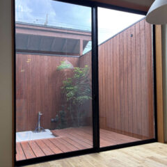 Interior room with a large glass sliding door opening to a wooden courtyard, showing a small tree and outdoor deck.