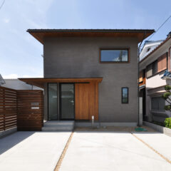 Front view of a modern two‑story gray house with a wooden entry door and a concrete driveway with gravel strips on either side.