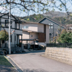 Residential street in a quiet Japanese neighborhood with modern houses and a hillside in the distance.
