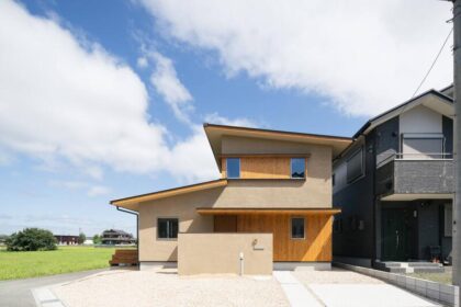 Front view of a modern, beige two-story house with wooden panels and a gravel driveway under a blue sky.