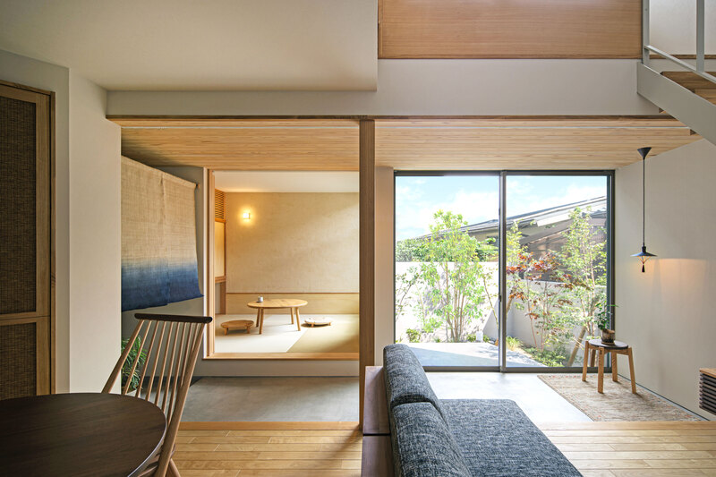 Open living area with a gray sofa facing a sliding glass door to a garden; a tatami room with a low table is visible.